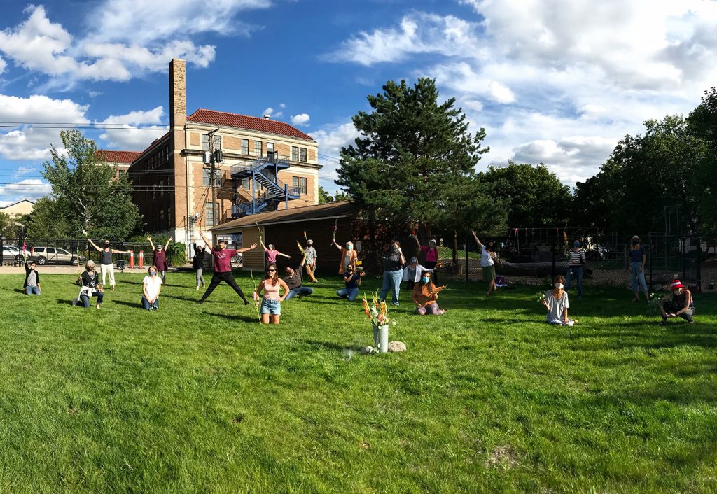 CLWS staff members stand with arms outstretched on the new green grassy field, celebrating the beginning of another school year and our beautiful grassy field!