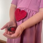 A tiny felted "love bug" is held carefully by two small hands