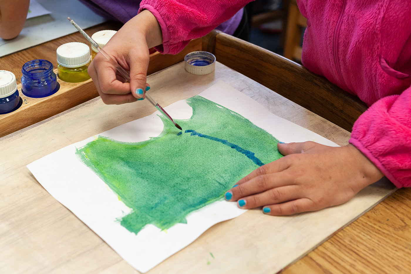 A fourth grade student uses watercolors to paint a map of Minnesota.