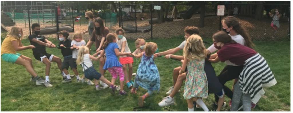 First graders play "tug of war" outdoors with their eighth grade buddies.